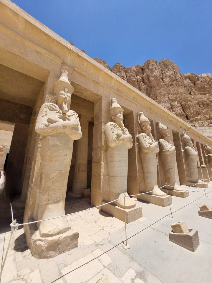 A row of sandstone statues of pharaohs lines the colonnade of an ancient Egyptian temple.
