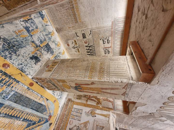 An ornately painted stone pillar stands in the middle of a richly decorated burial chamber.