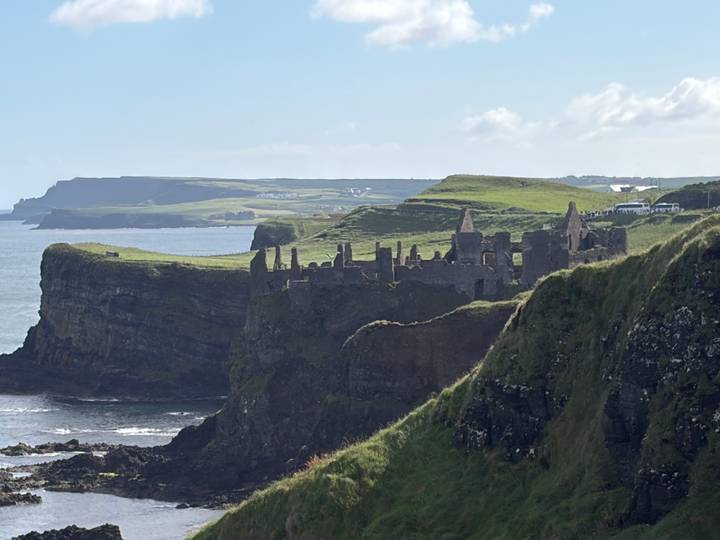 Ruins of Dunluce Castle perched on dramatic green cliffs above the Atlantic with layered headlands beyond.