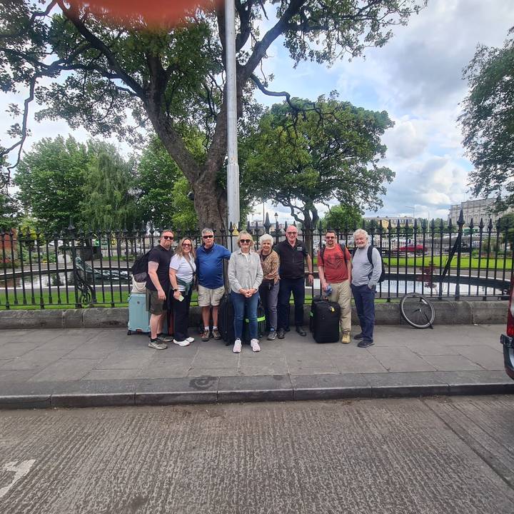 Tour group with suitcases gathers on a Dublin street beside an iron fence and small fountain.