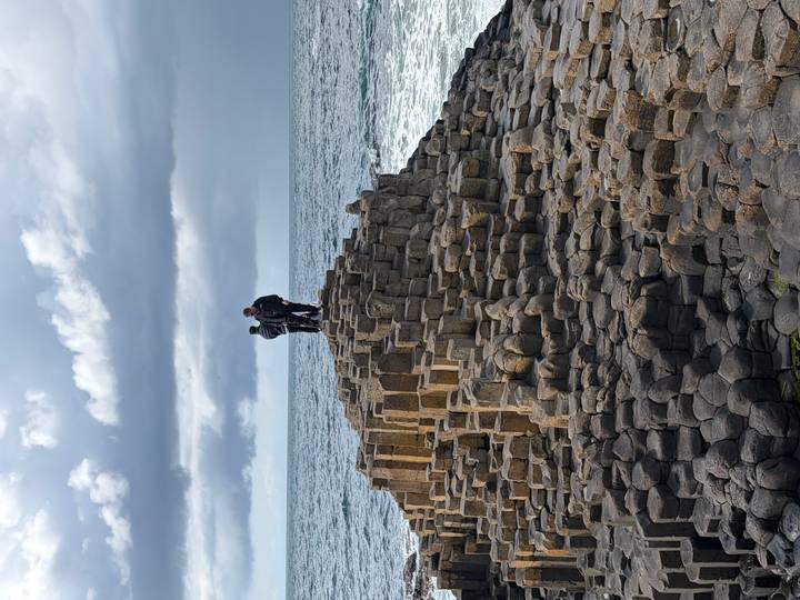 People stand atop the interlocking basalt columns of the Giant's Causeway as waves crash below.