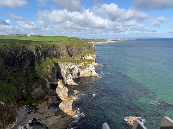 Expansive aerial view of rugged green cliffs meeting turquoise sea under a partly cloudy sky.