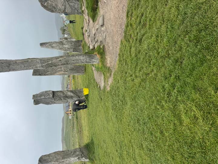 A caretaker tends the ancient standing stones of Callanish on a misty grass plain.