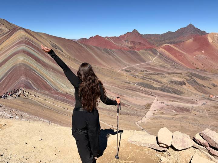 A woman triumphantly raises her arm at the colourful striped slopes of Rainbow Mountain in Peru.
