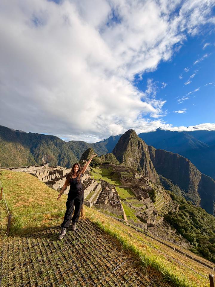 Panoramic view of Machu Picchu ruins framed by dramatic green peaks under a partly cloudy sky.