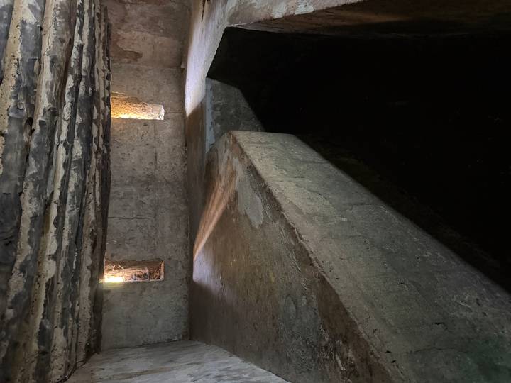Dimly lit stone chamber with narrow windows and stagnant dark water filling a sunken area.