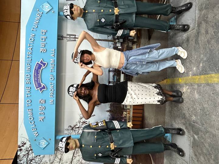 Two visitors wearing helmets pose beneath a sign for the 3rd Infiltration Tunnel at the DMZ.