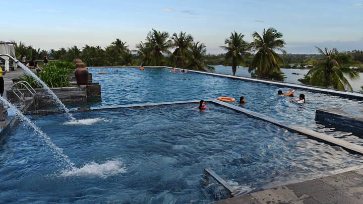 Infinity pool overlooking river and palm trees with guests swimming at dusk.