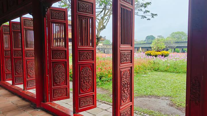 Intricately carved red wooden doors of Hue Imperial Citadel framing a flower garden.