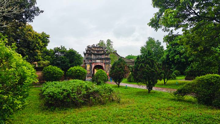 Ancient moss-covered gate of a royal tomb complex surrounded by lush gardens after rain in Hue.