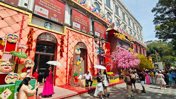 Colorful storefronts with lanterns, flowers and crowds celebrating outside a decorated building.