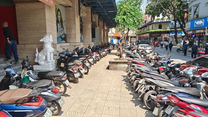 Long row of parked motorbikes lining a busy urban sidewalk in Vietnam.