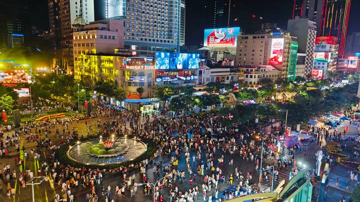 Crowded Nguyen Hue Walking Street in Ho Chi Minh City illuminated with neon lights and billboards at night.