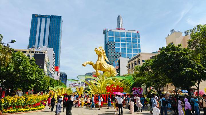 Bustling pedestrian street with towering golden stallion Tet sculpture, modern skyscrapers, and festive crowds.