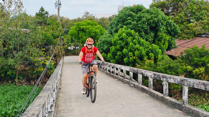 Cyclist crossing narrow concrete bridge over lush green canal in rural Vietnam.