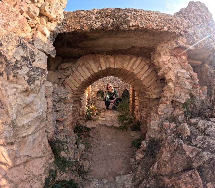 A traveller crouches inside a small stone archway of ancient ruins surrounded by rugged masonry.