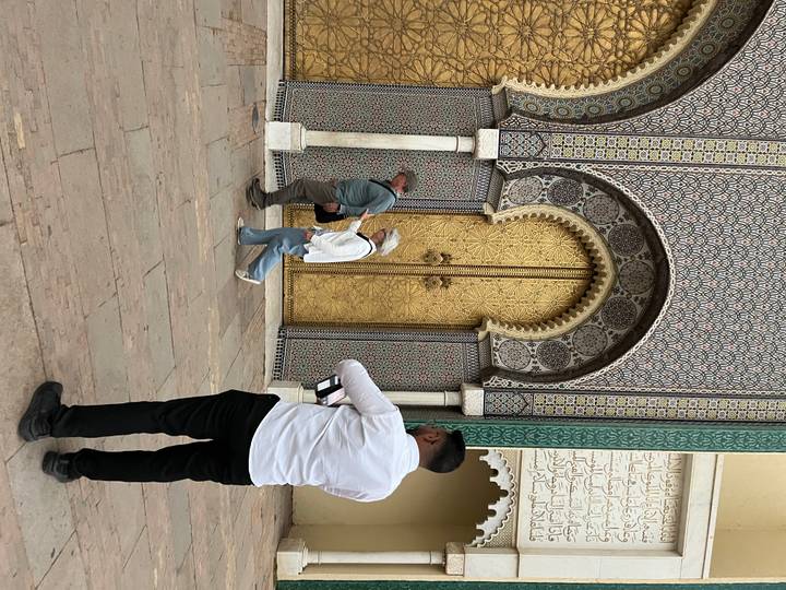 Close-up of tourists examining one of the ornate golden palace doors with intricate tile borders in Fes.