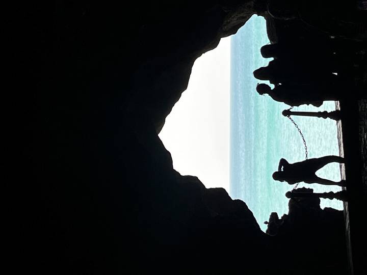 Silhouetted visitors inside Hercules Cave looking out to turquoise Atlantic waters near Tangier.
