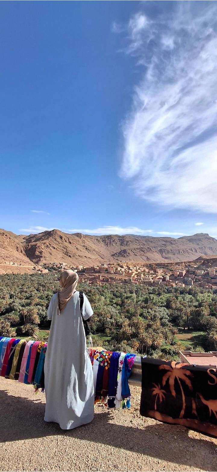 Traveler admiring panoramic view of palm oasis and rugged mountains near Dades Valley.