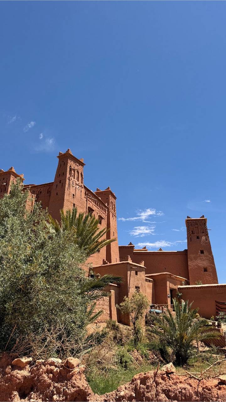 Red clay kasbah towers of Ait Benhaddou against clear blue sky.