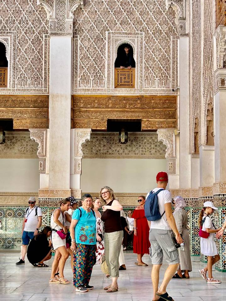 Tour group gathered in ornate courtyard with carved arches and mosaic tiles inside a historic Moroccan monument
