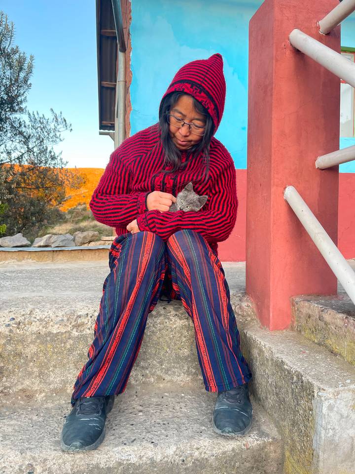Local woman in colorful knit sweater holding small kitten while seated on stone step on Lake Titicaca island
