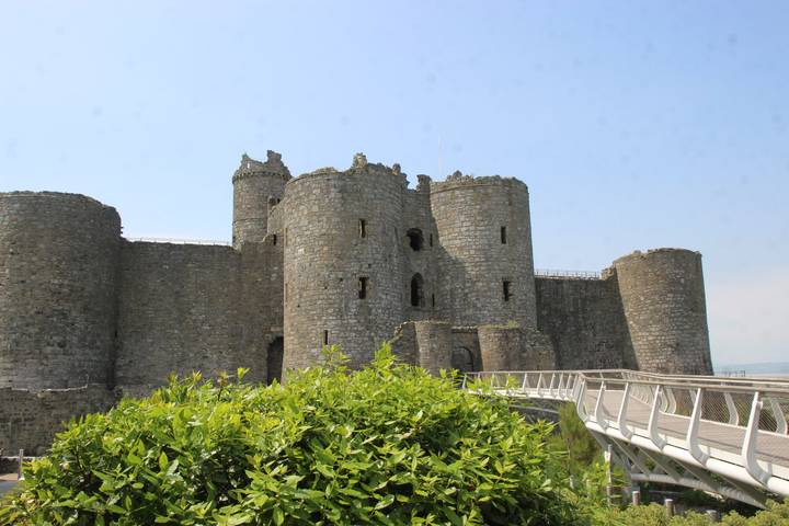 Medieval stone Pembroke Castle with round towers rising above greenery and modern walkway.