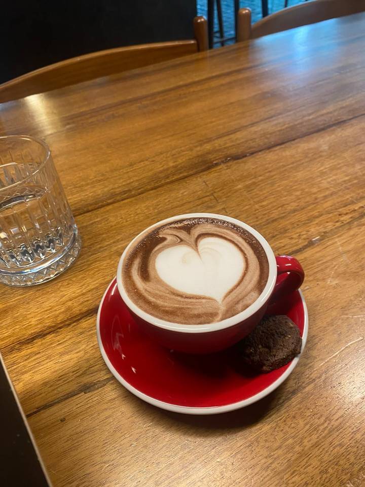 Cup of hot chocolate with heart-shaped latte art on wooden table beside a glass of water