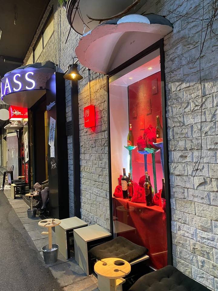 Evening street view of a stone-clad wine bar with illuminated red sign and bottle display