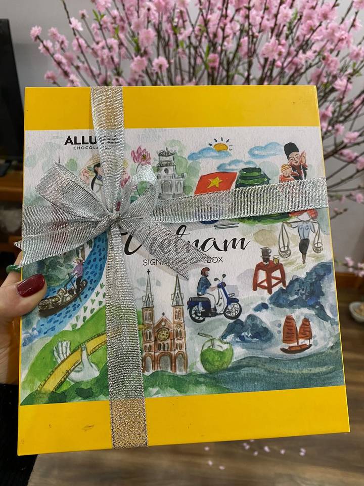 Hand holding a ribbon-wrapped chocolate gift box illustrated with Vietnam landmarks