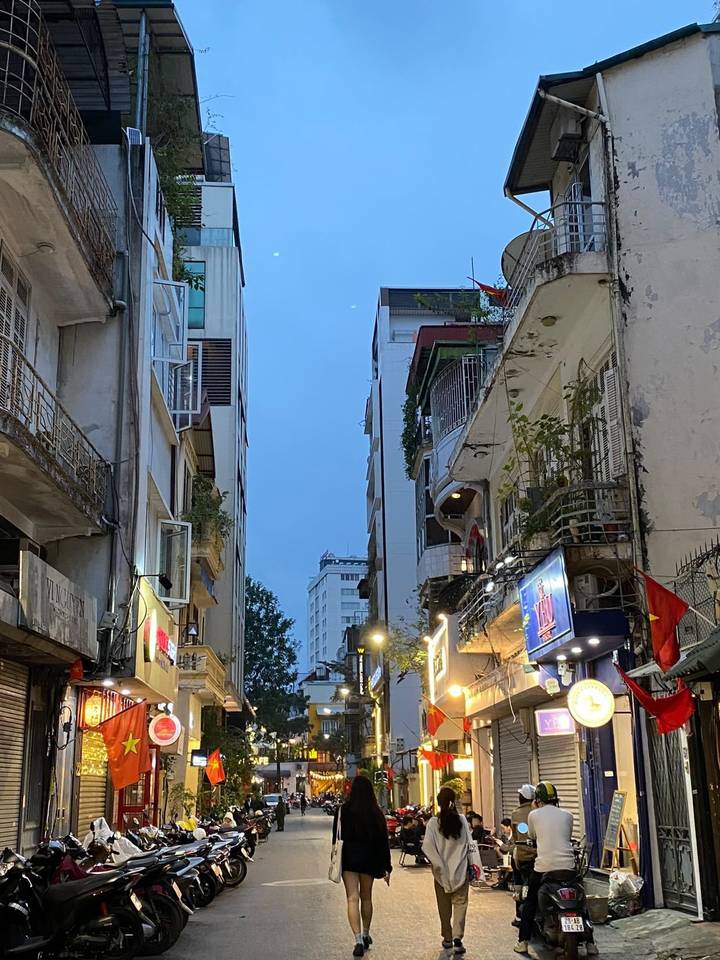 Twilight urban alley in Hanoi lined with narrow balconies and Vietnamese flags