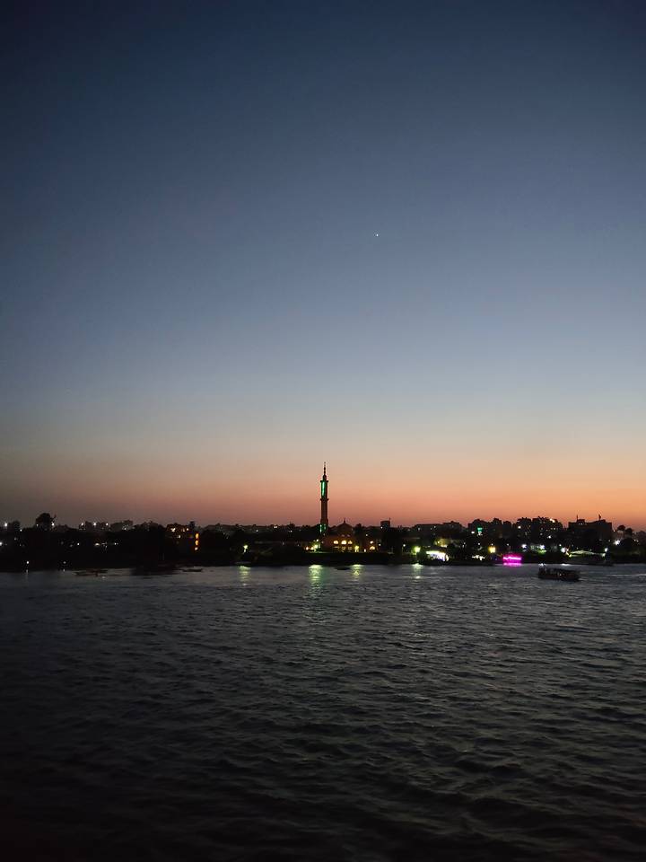 Sunset over the Nile River with city skyline and single illuminated minaret silhouetted against colorful sky
