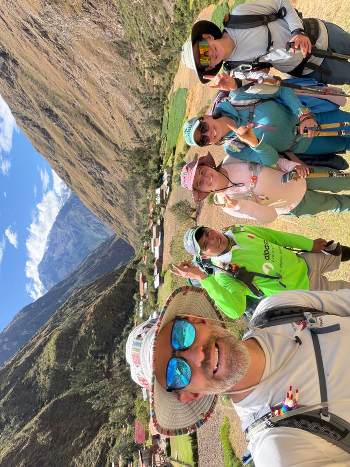 Guided group of hikers pose with trekking poles in a verdant Andean valley beneath jagged peaks