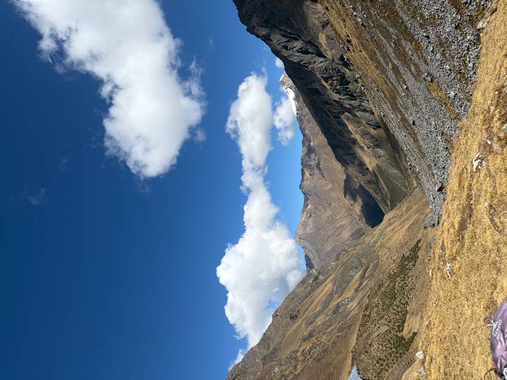 Wide high-altitude valley with rugged brown slopes and bright blue sky dotted with clouds