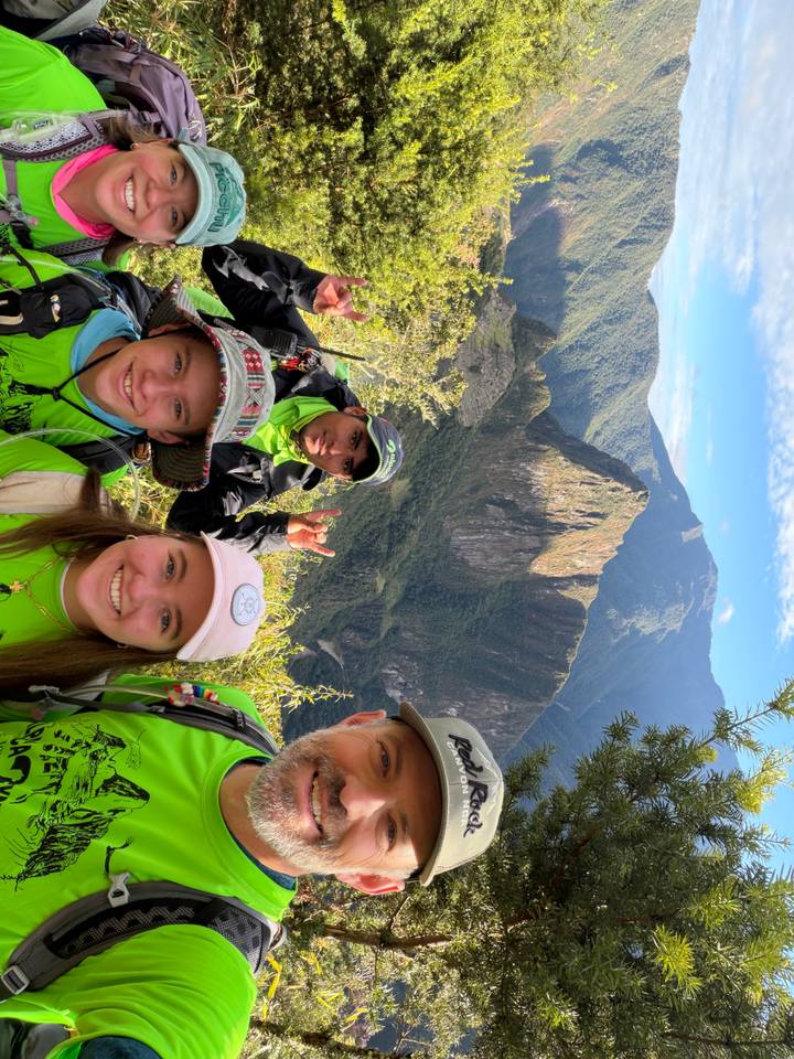 Happy trekkers in bright green shirts pose with Huayna Picchu towering behind lush forest