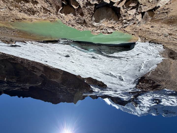 Glacial tongue descends steep rock face into turquoise meltwater pool high in Andes
