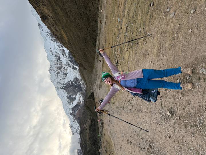 Cheerful hiker raises trekking poles triumphantly on snowy valley trail beneath glacier