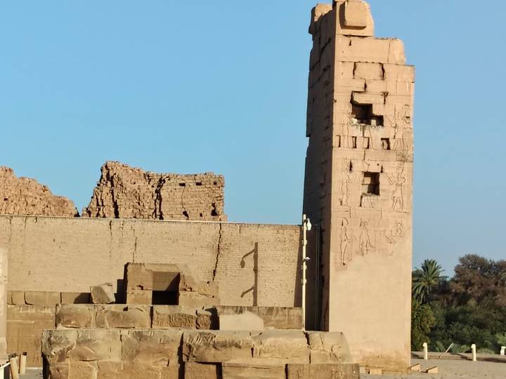 Ancient stone walls and a slender obelisk against a clear blue sky at an Egyptian temple