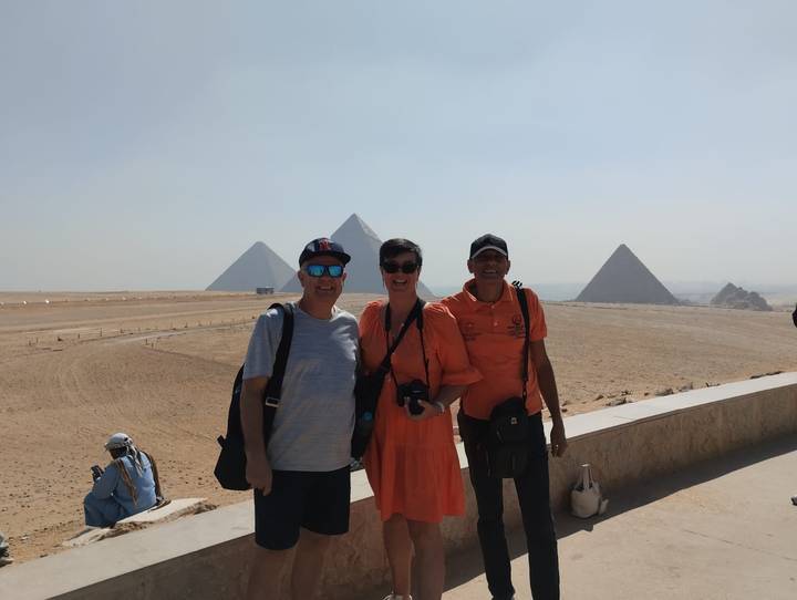 Travellers smiling in front of the pyramids on a bright desert morning