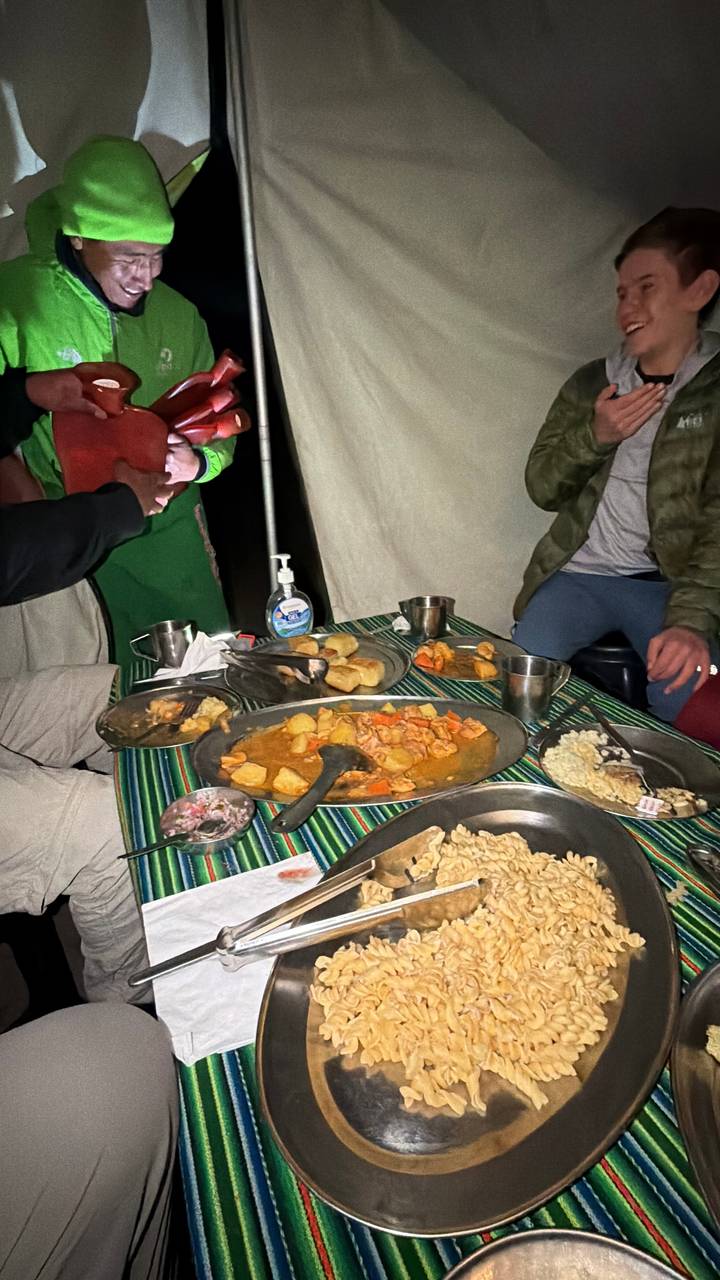 Campsite dinner scene with metal trays of stew and vegetables on a striped tablecloth inside a tent