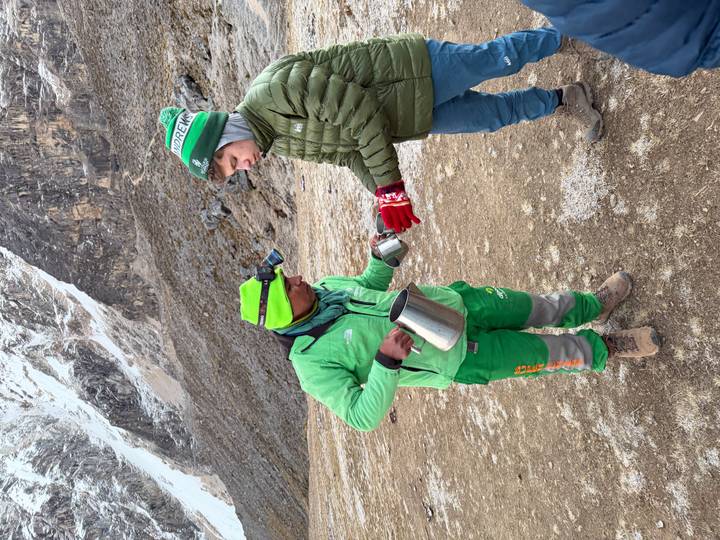 Guide serving a hot drink to a trekker on a frosty mountain morning