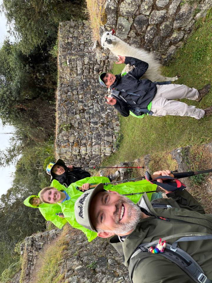 Playful group peeking from behind stone wall ruins wearing rain ponchos