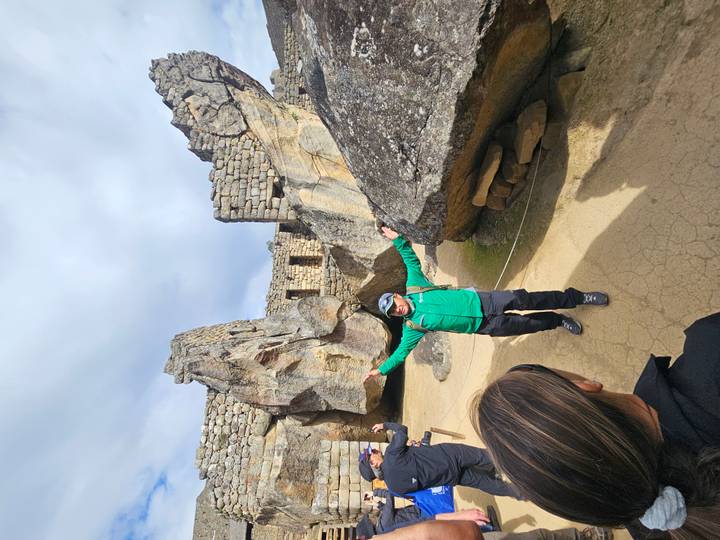 A lively guide spreads his arms while lecturing among giant carved stones at Machu Picchu.