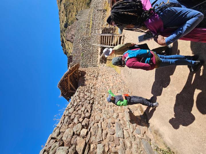 A guide gestures toward stone terraces at an Inca archaeological site under a deep blue sky.