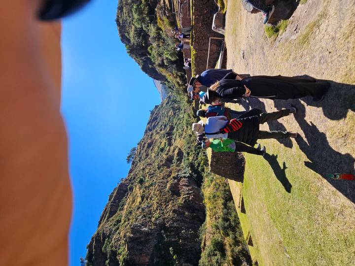 Tourists listen to a guide at an Inca site, though a finger partly obscures the top of the frame.