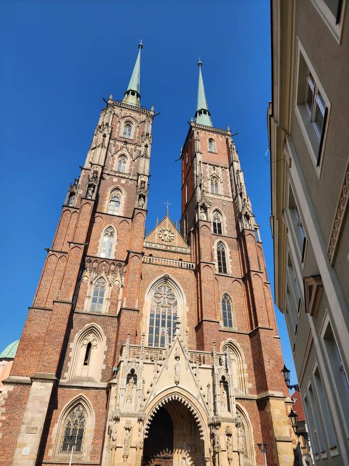 Twin brick Gothic towers of a cathedral rise sharply into a cloudless blue sky, highlighting detailed tracery.
