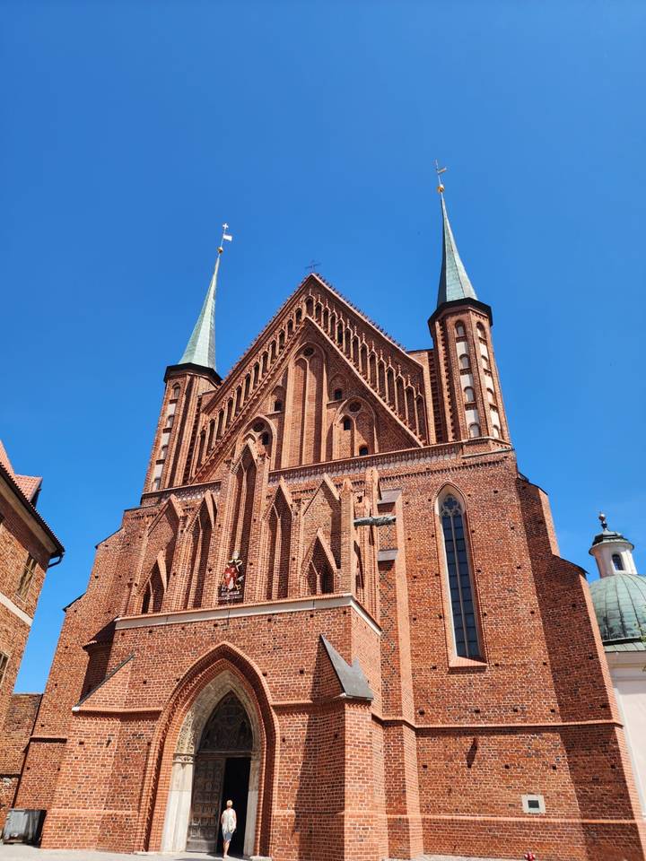 Brick Gothic church with sharp spires stands out against a vibrant blue sky in a Polish old town.