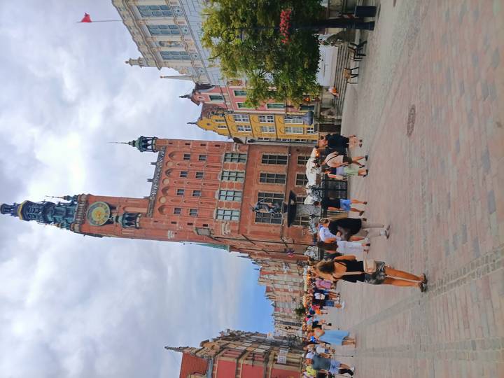 Lively pedestrian street in Gdansk lined with ornate colourful buildings and crowned by a tall town hall tower.