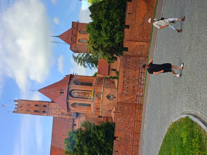Red-brick castle complex with tower and fresco sits behind fortified walls while visitors walk the cobblestone court.