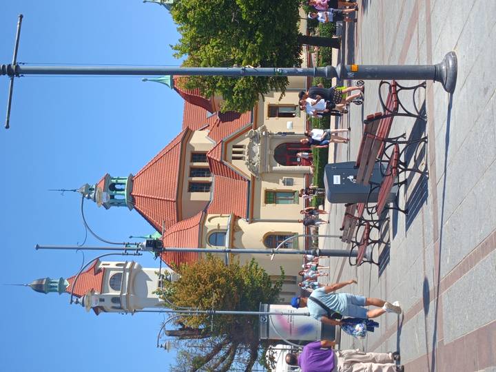 Historic spa house with red-tiled roof and turrets anchors a sunny pedestrian plaza filled with visitors.